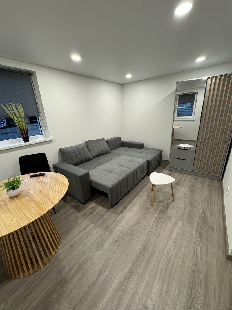 Kambarys po remonto Žaliakalnyje: kampinė sofa, apvalus stalas, įleidžiami šviestuvai